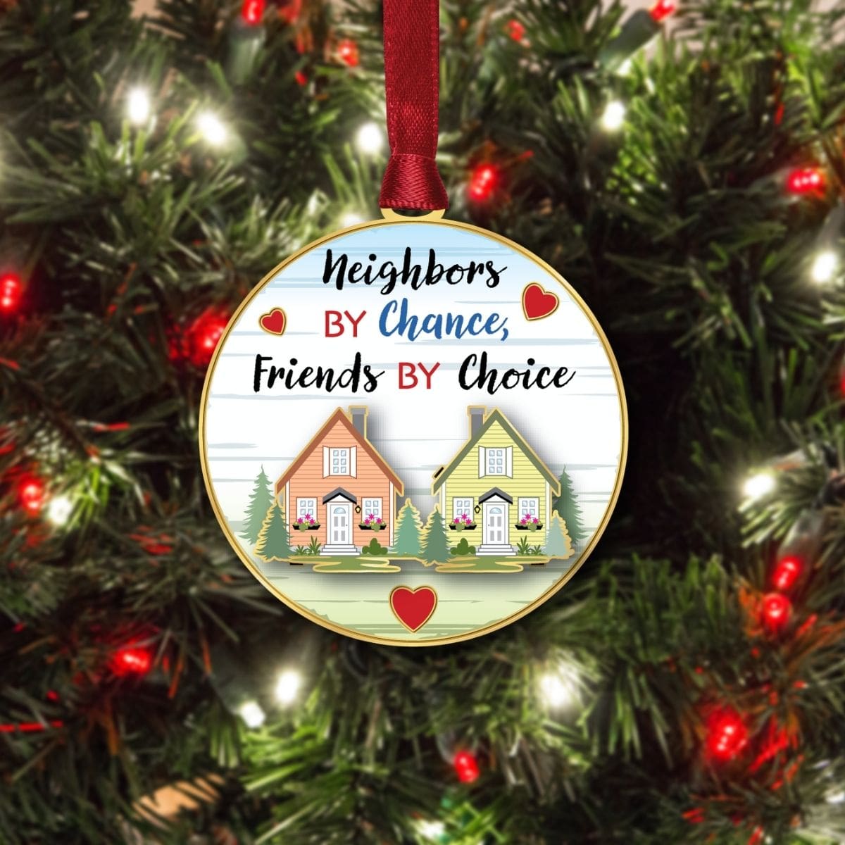 “Neighbors by Chance, Friends by Choice” ornament from Beacon Design hanging on a Christmas tree, featuring two homes, hearts, and a friendship message.