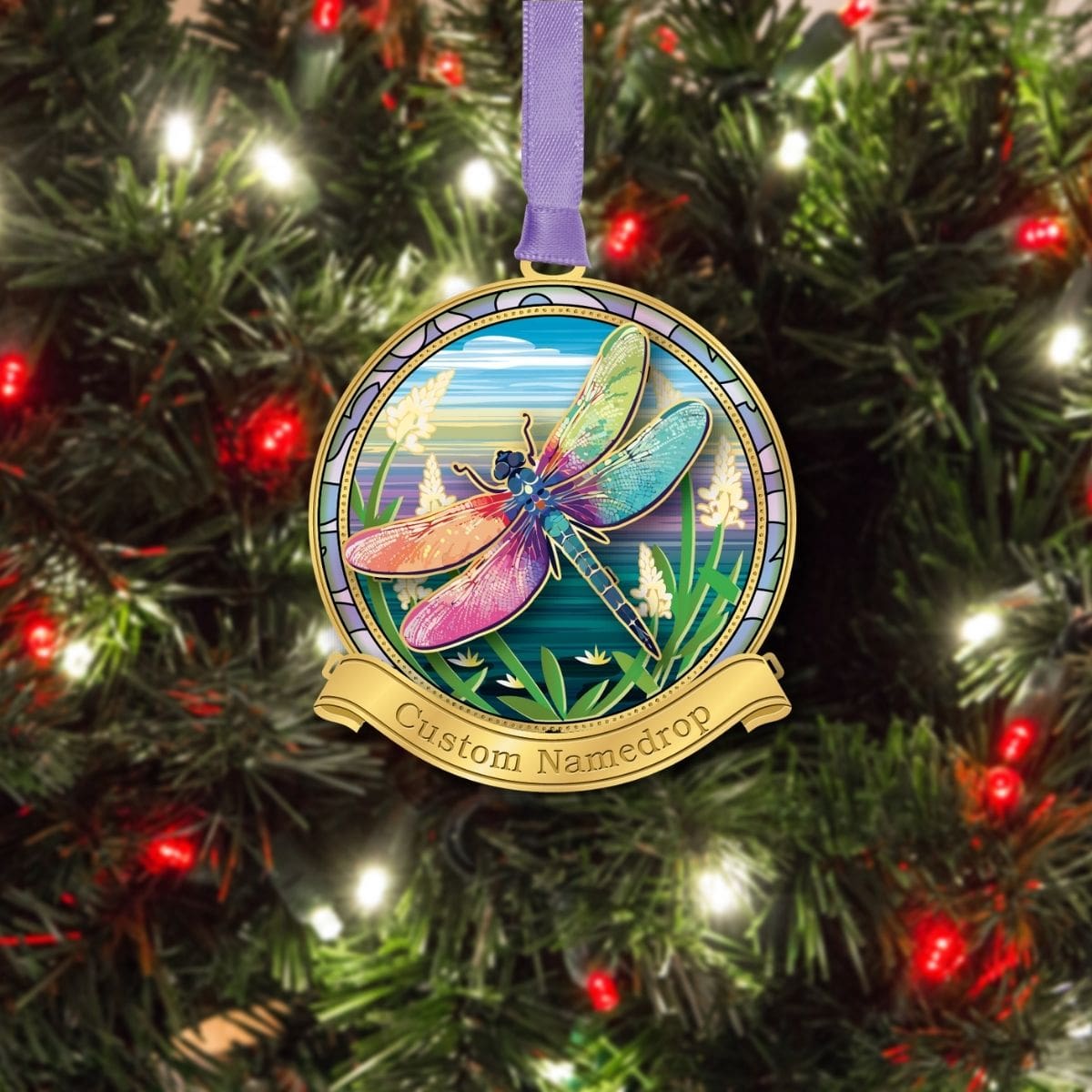 Dragonfly namedrop ornament from Beacon Design hanging on a Christmas tree, featuring a colorful dragonfly with multicolored wings over a nature scene and a customizable banner.