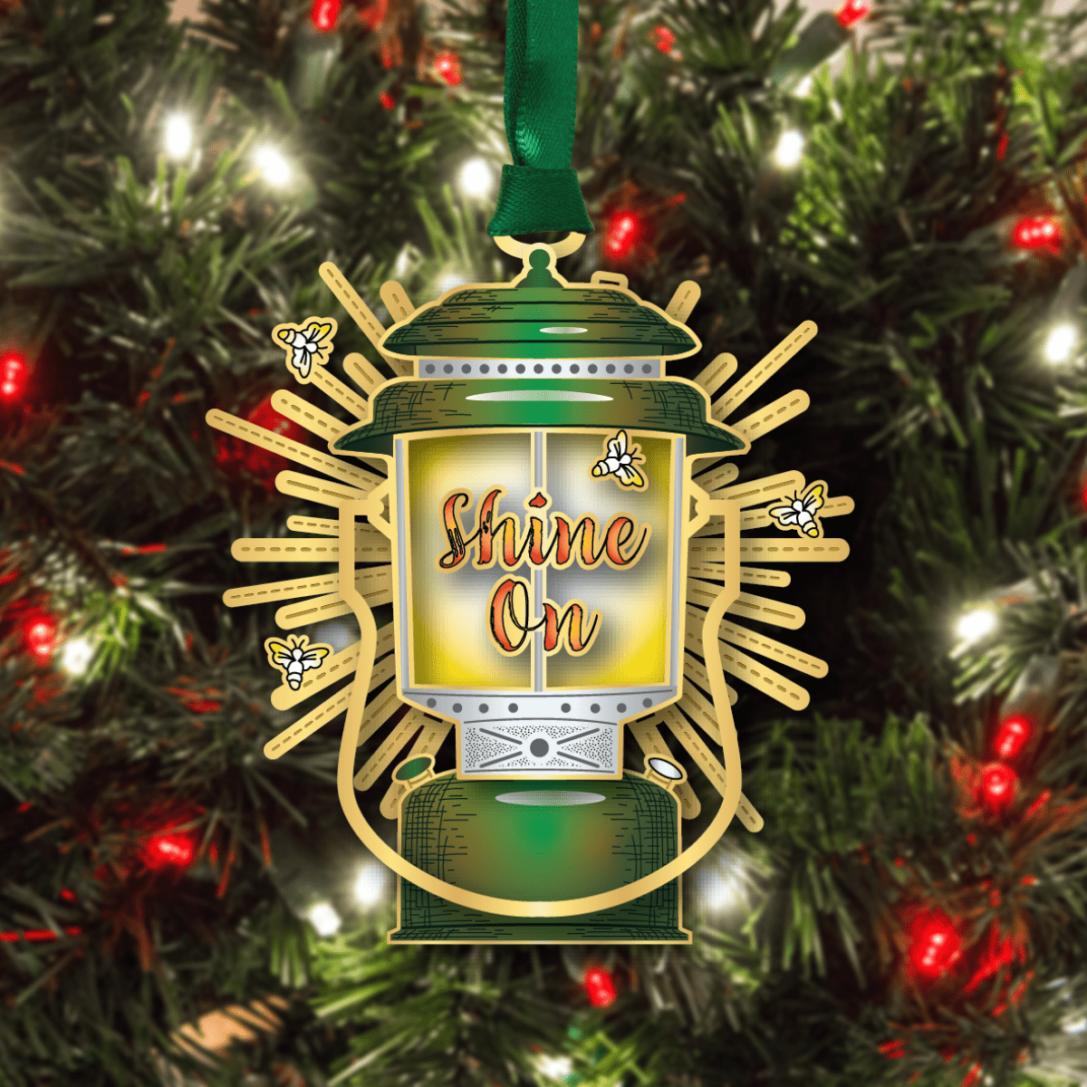 Custom ornament featuring a vintage lantern surrounded by bees and sunburst accents with the phrase “Shine On,” displayed on a decorated Christmas tree